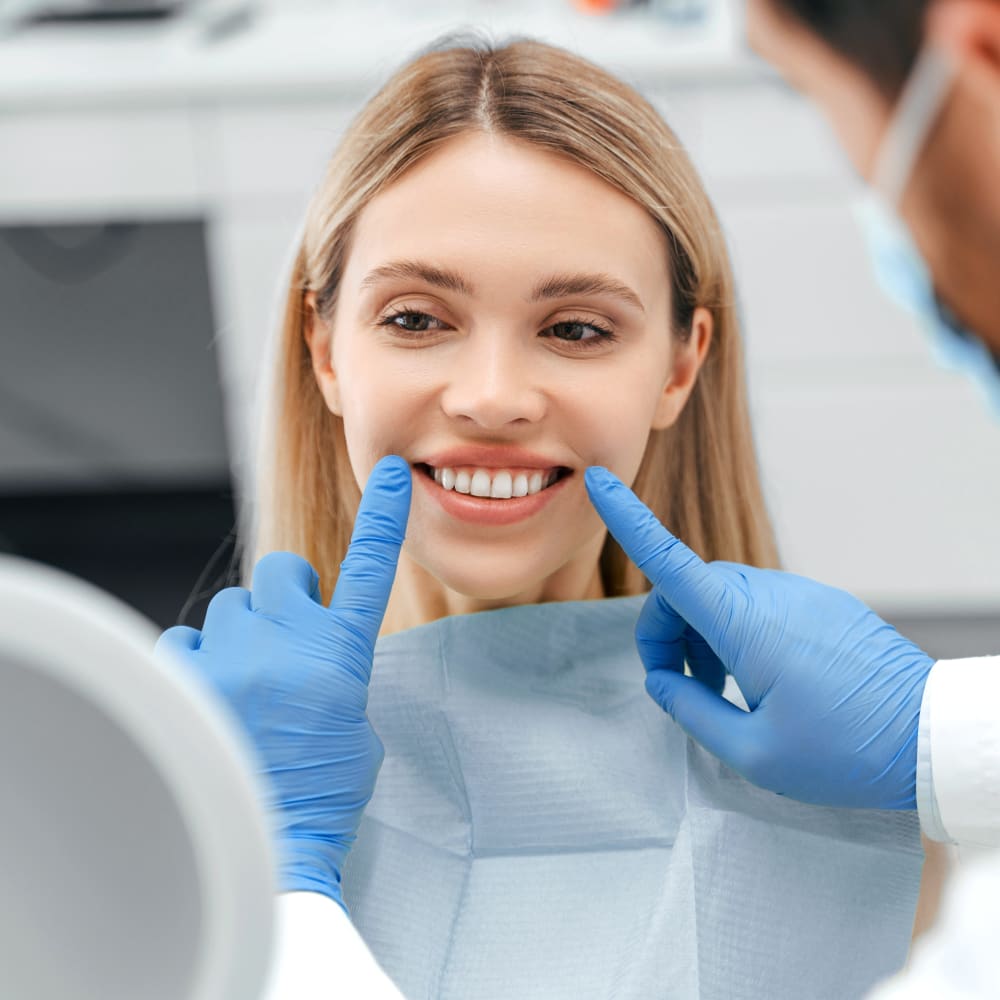 A young woman sits in the chair at the orthodontist office while the dental professional points to either side of her smile.