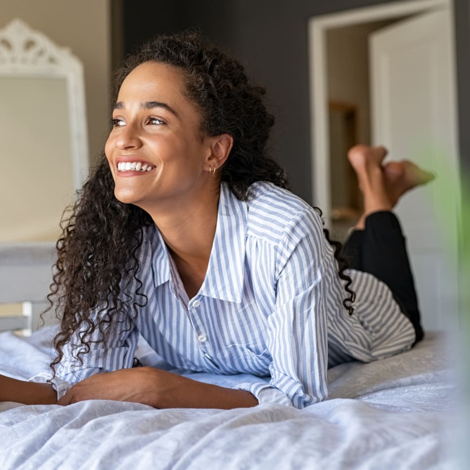 A woman lays on her stomach on a bed, smiling and looking off to the side.