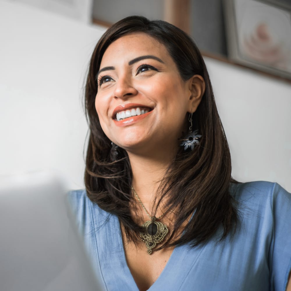 A woman with long dark hair sits inside and looks ahead of her, smiling wide.