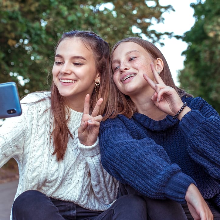 Two teenager girls are taking a selfie with a phone while doing peace signs