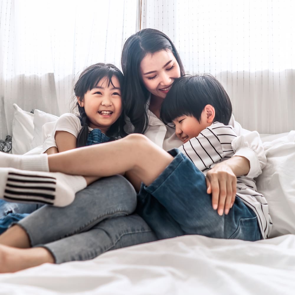 A woman and two small children cuddle up on a bed. They are all smiling.
