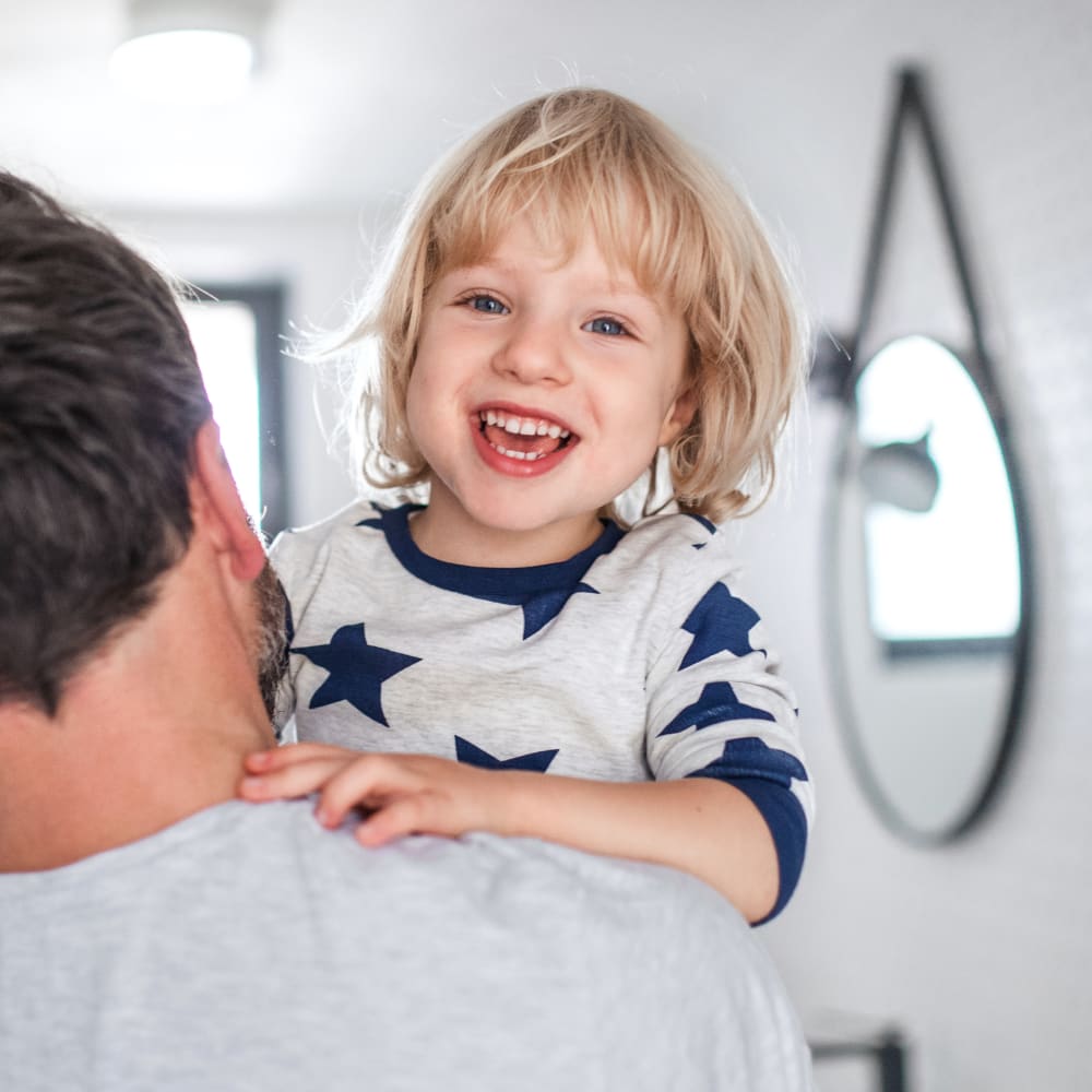 A small boy is being held by a man. The boy is resting his arm on the man's shoulder and smiling at the camera.
