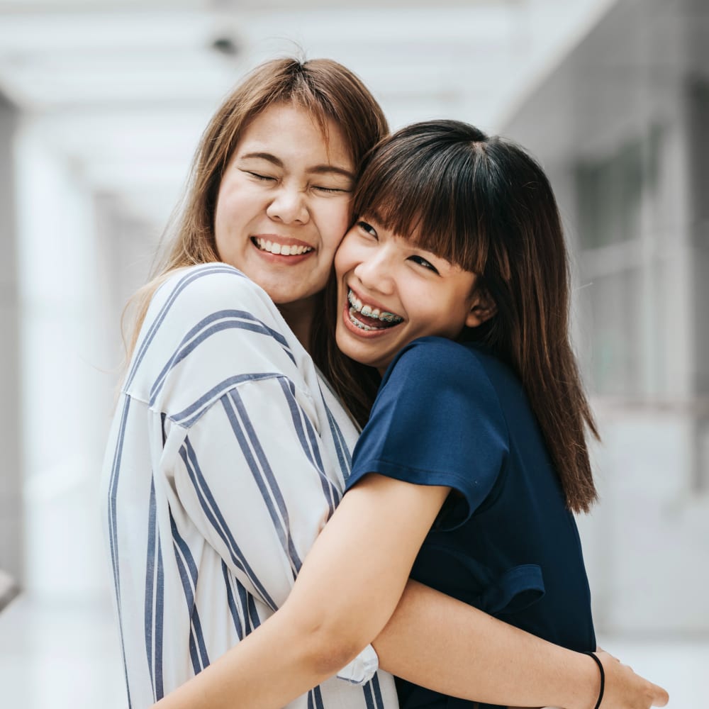 Two teen girls hug eachother and smile. One has braces.