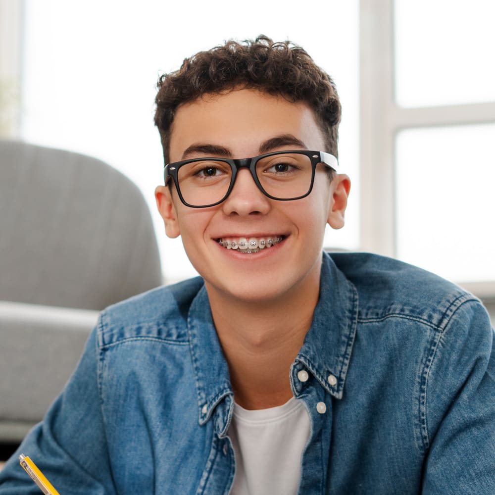 A teen boy wearing glasses and braces look at the camera and smiles.